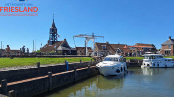 Tussen water en historie: een betoverend uitzicht op Hindeloopen met de iconische ophaalbrug en de statige toren die het eeuwenoude verhaal van deze Friese stad vertellen.