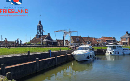 Tussen water en historie: een betoverend uitzicht op Hindeloopen met de iconische ophaalbrug en de statige toren die het eeuwenoude verhaal van deze Friese stad vertellen.